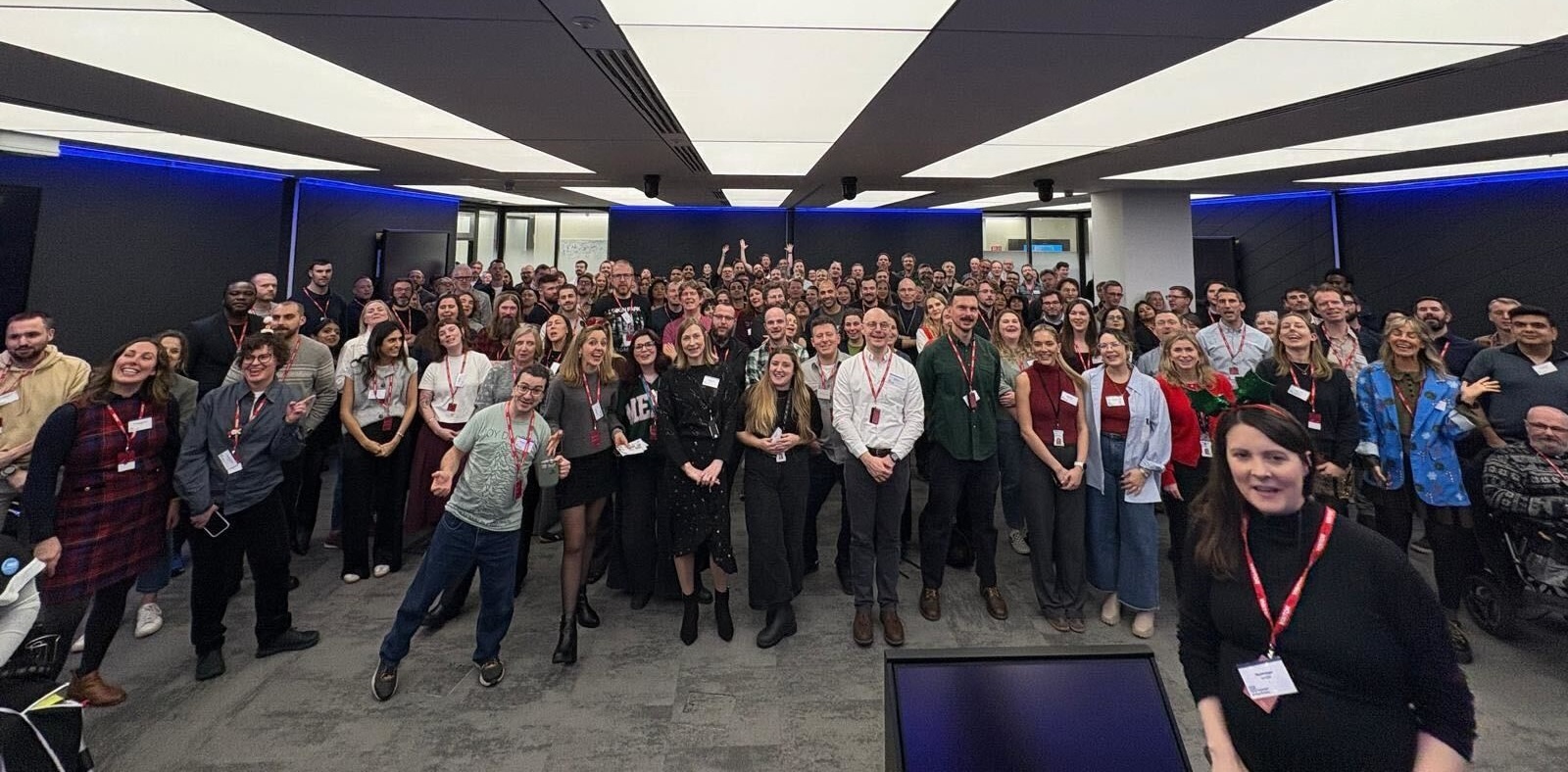Photo of a large group of about 100 people smiling at the camera in a conference room