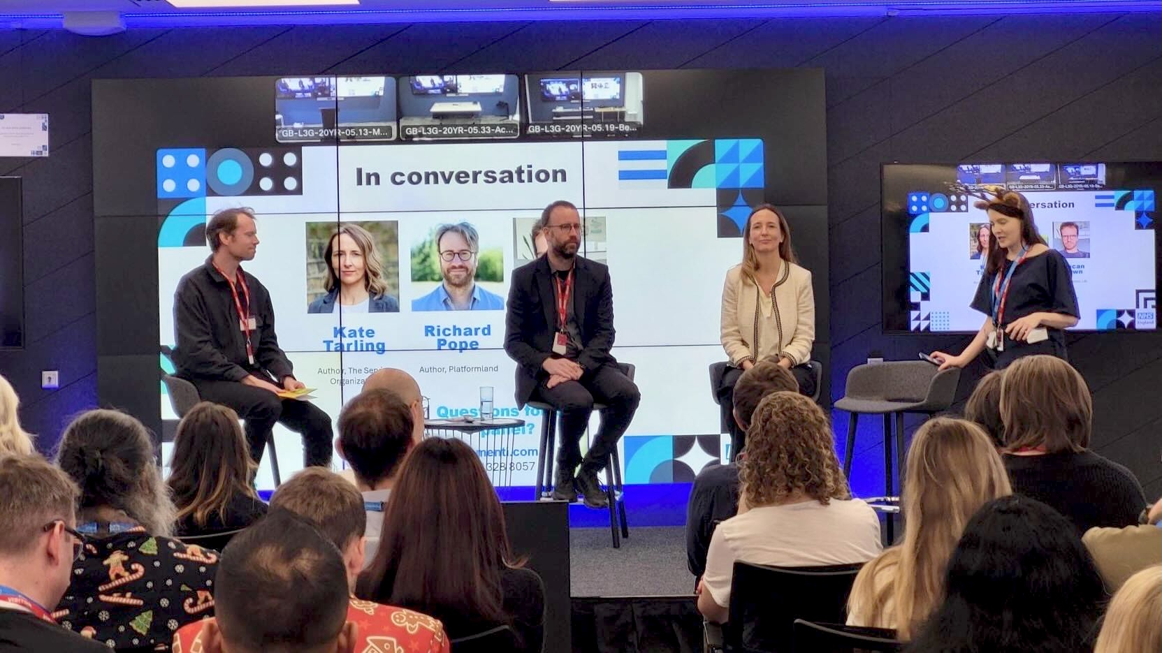 Photo of 4 people sat on stools on a stage in front of a screen saying In conversations with Kate Tarling and Richard Pope