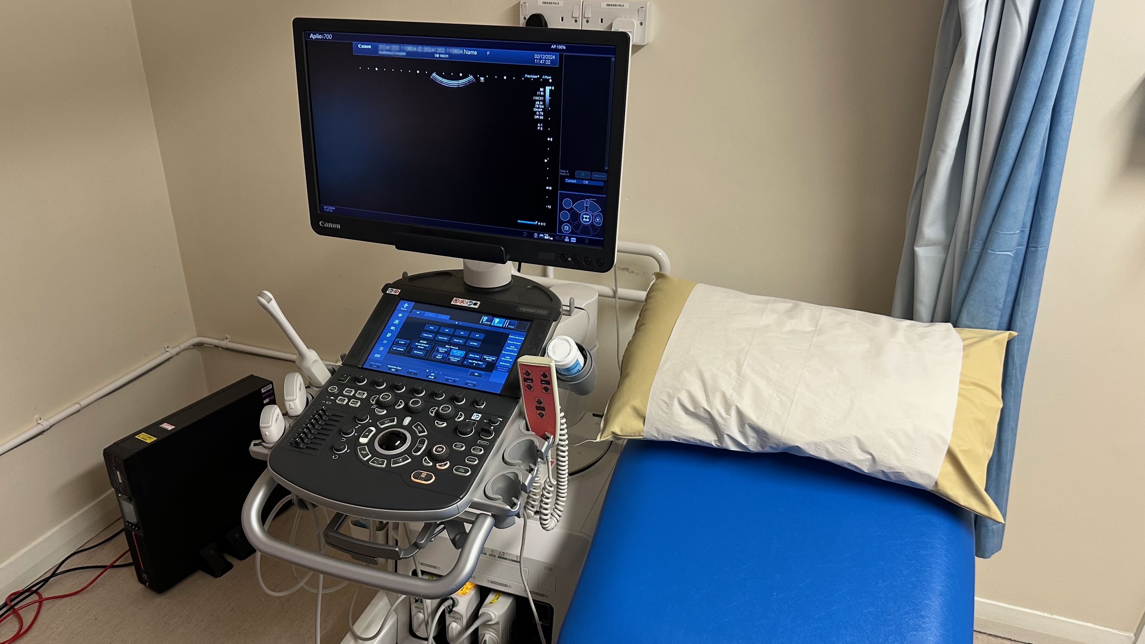 Photo of a maternity ultrasound machine in a small room next to an empty blue reclining seat with a pillow