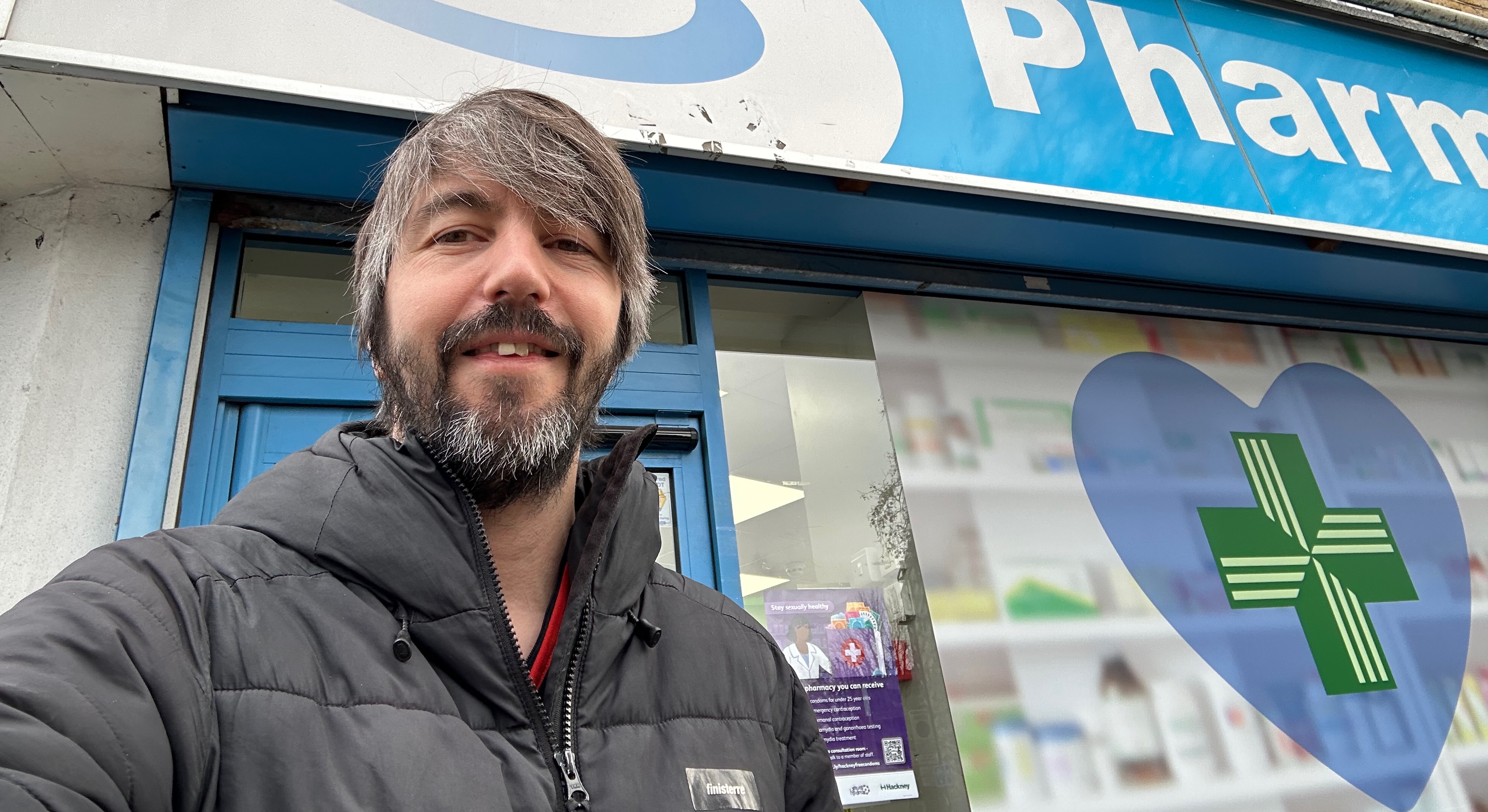 Photo of me stood outside a pharmacy, wrapped up in a warm coat