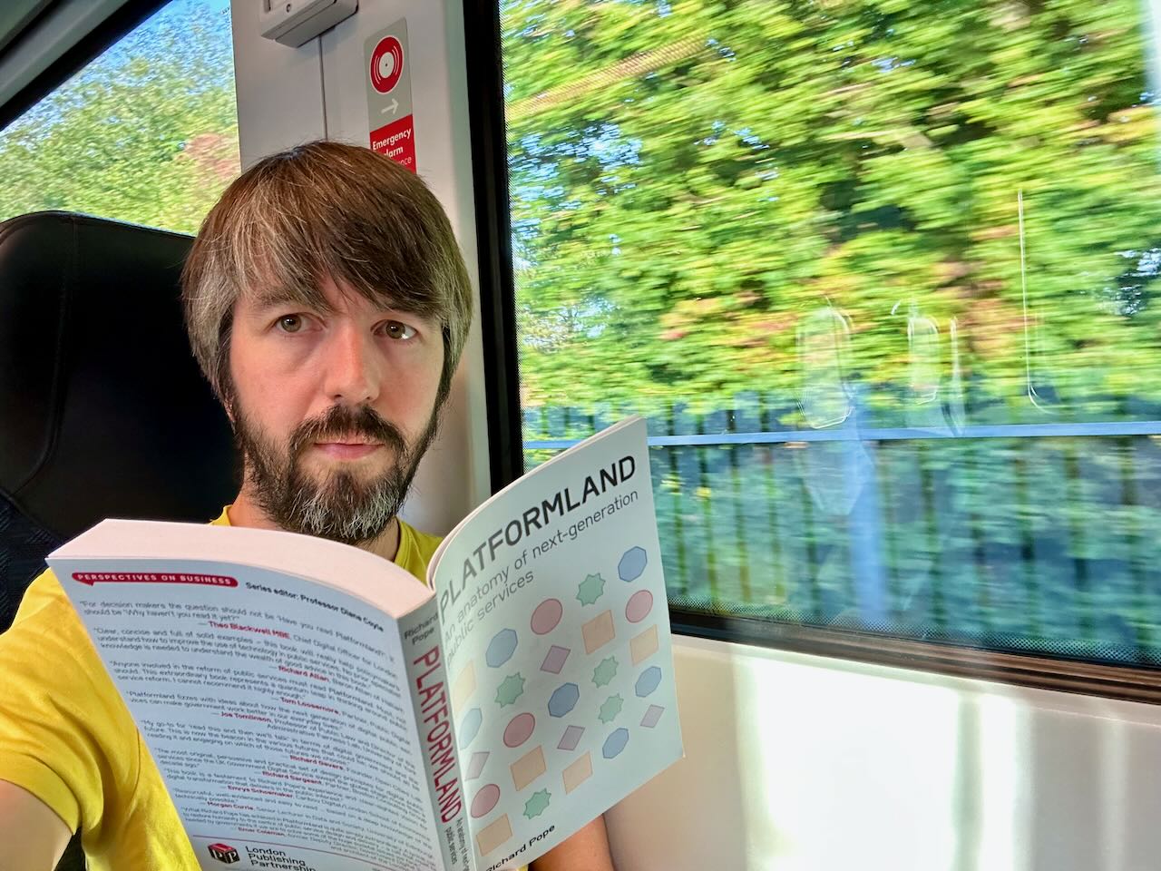 Photo of me on a train reading a book titled 'Platformland: An anatomy of next generation services' by Richard Pope, which has a grid of different shapes in different colours on its cover