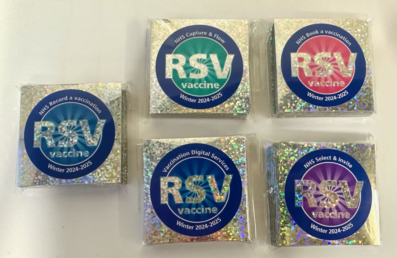 Photo of 5 packs of circular stickers, each of which is on shiny foil backing, with 'RSV vaccine' in big letters, and has the name of the team on the top, and 'Winter 2024-2025' at the bottom