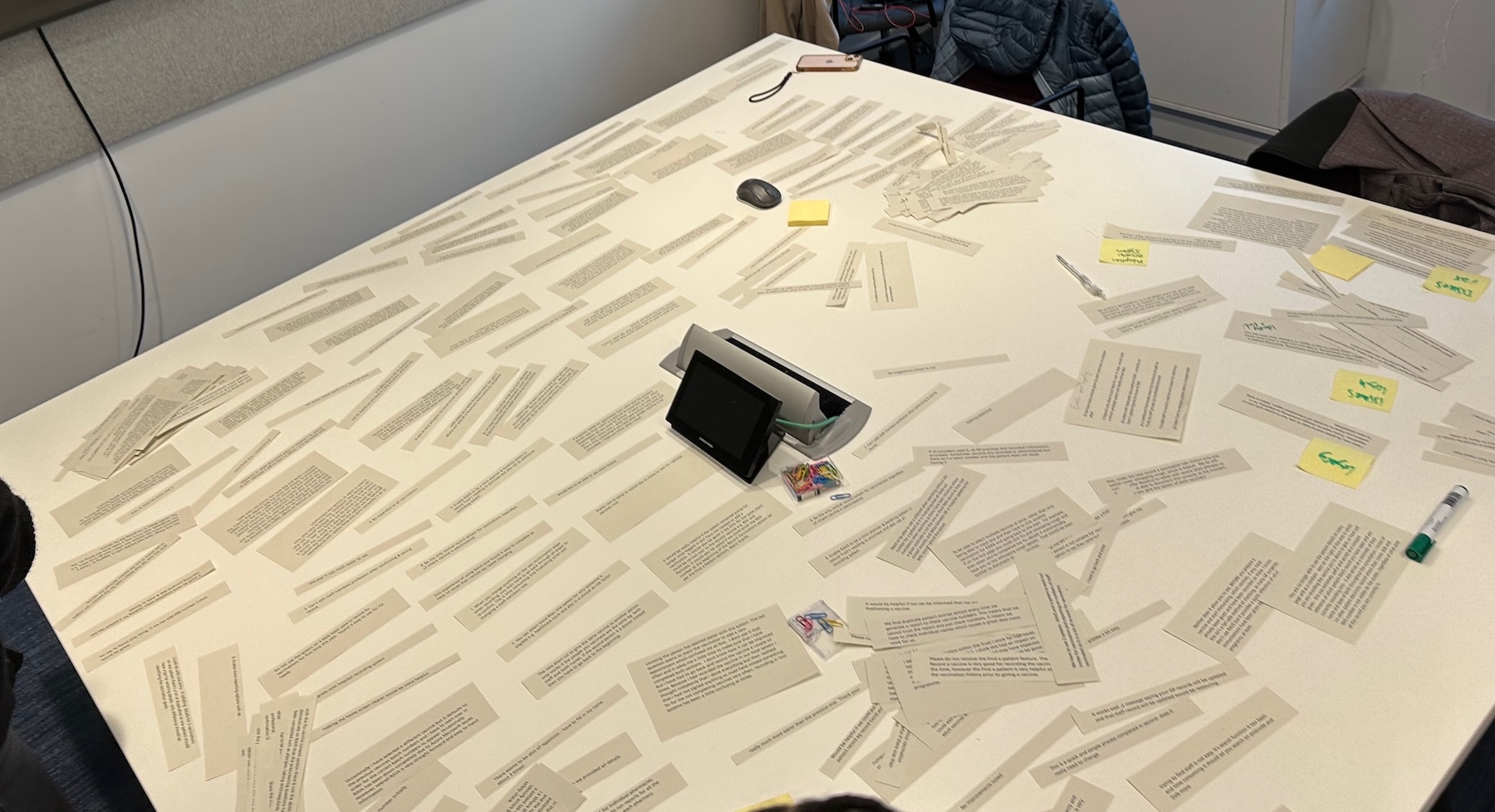 Photo of a table on which are scattered hundreds of strips of paper containing lines of text